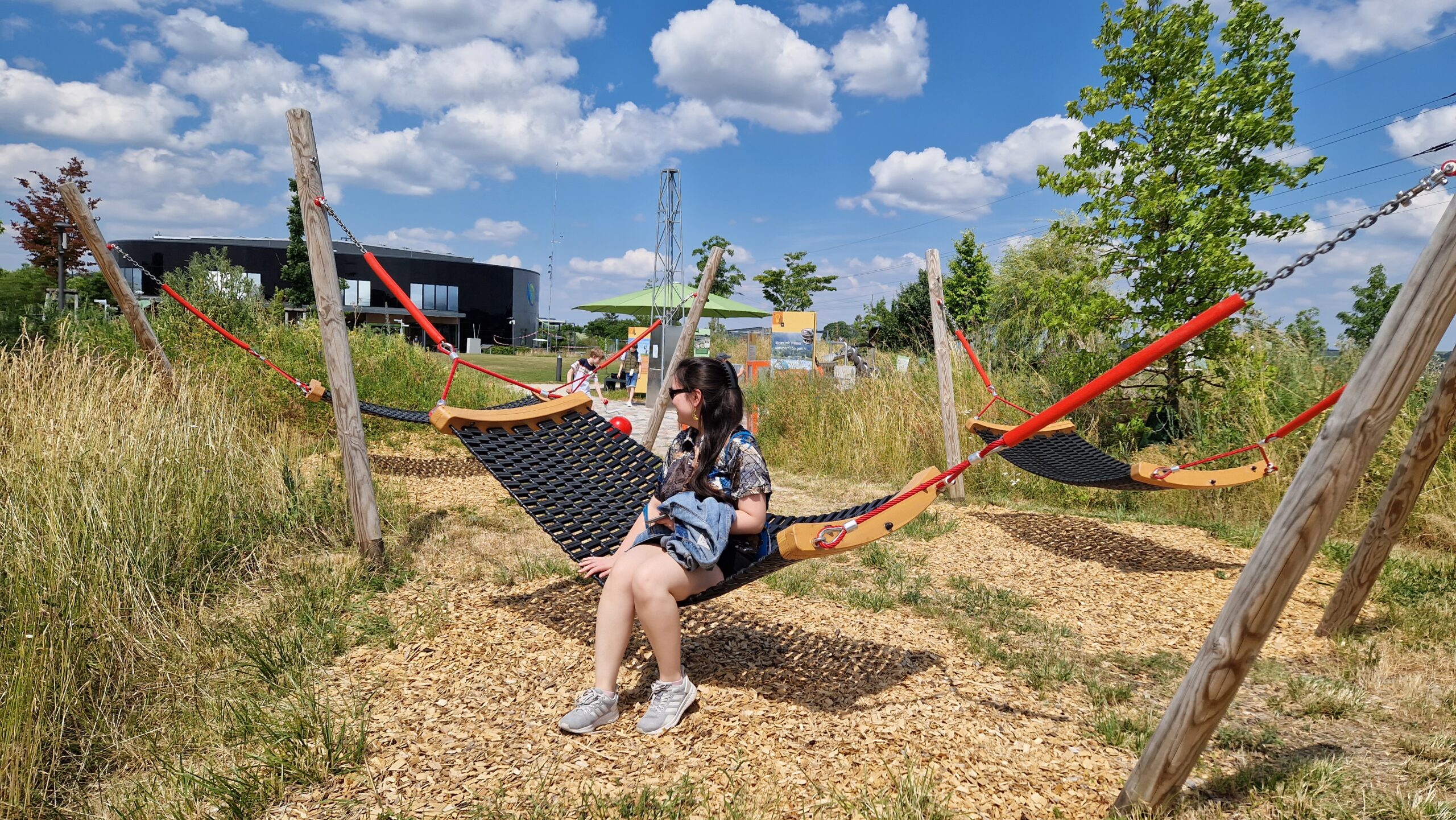Eine Kollegin sitzt auf einer Hängematte im Außenbereich der KLIMA ARENA, dem sogenannten Themenpark.